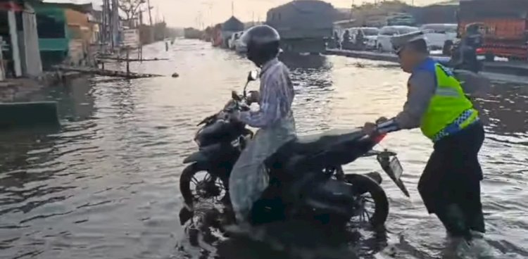 Anggota Satlantas Membantu Seorang Pengendara Sepeda Motor Yang Mogok Setelah Menerjang Genangan Rob Di Jalur Pantura Semarang-Demak. Tangkapan Layar